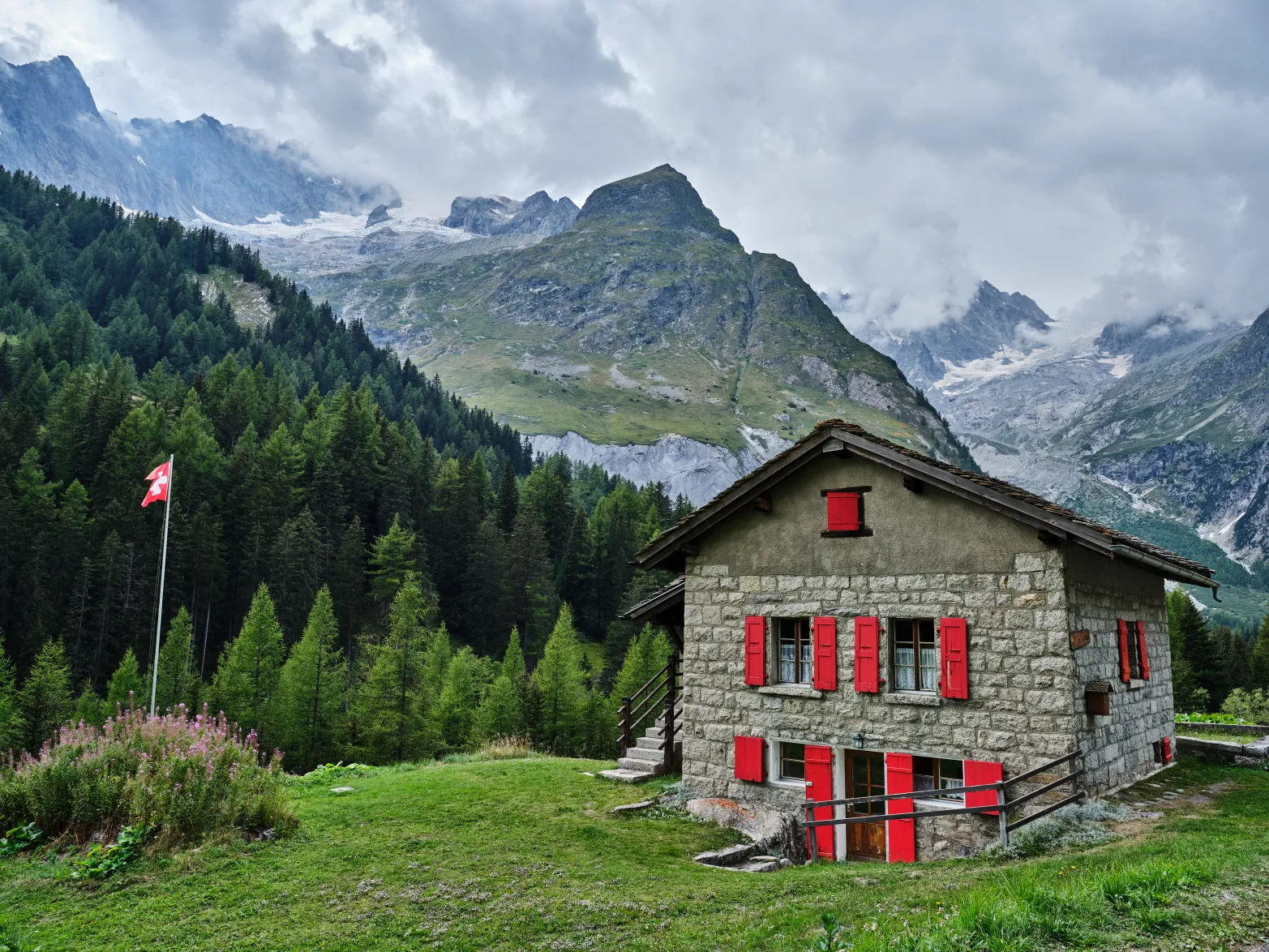 kamenný dům se švýcarskou vlajkou a zaledněnými horami v pozadí